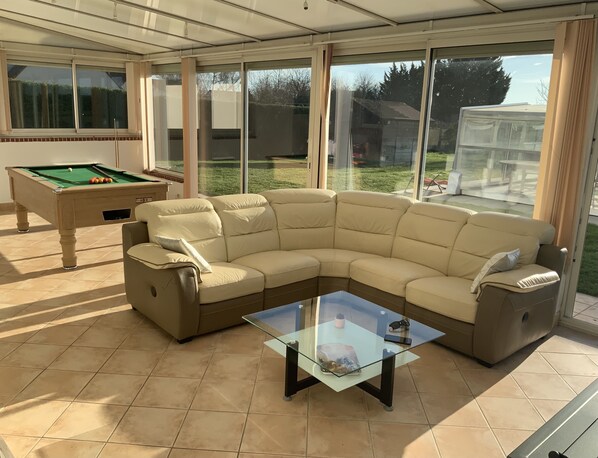 Una sala de estar con un sofá seccional color beige, una mesa de centro de vidrio y una mesa de billar.