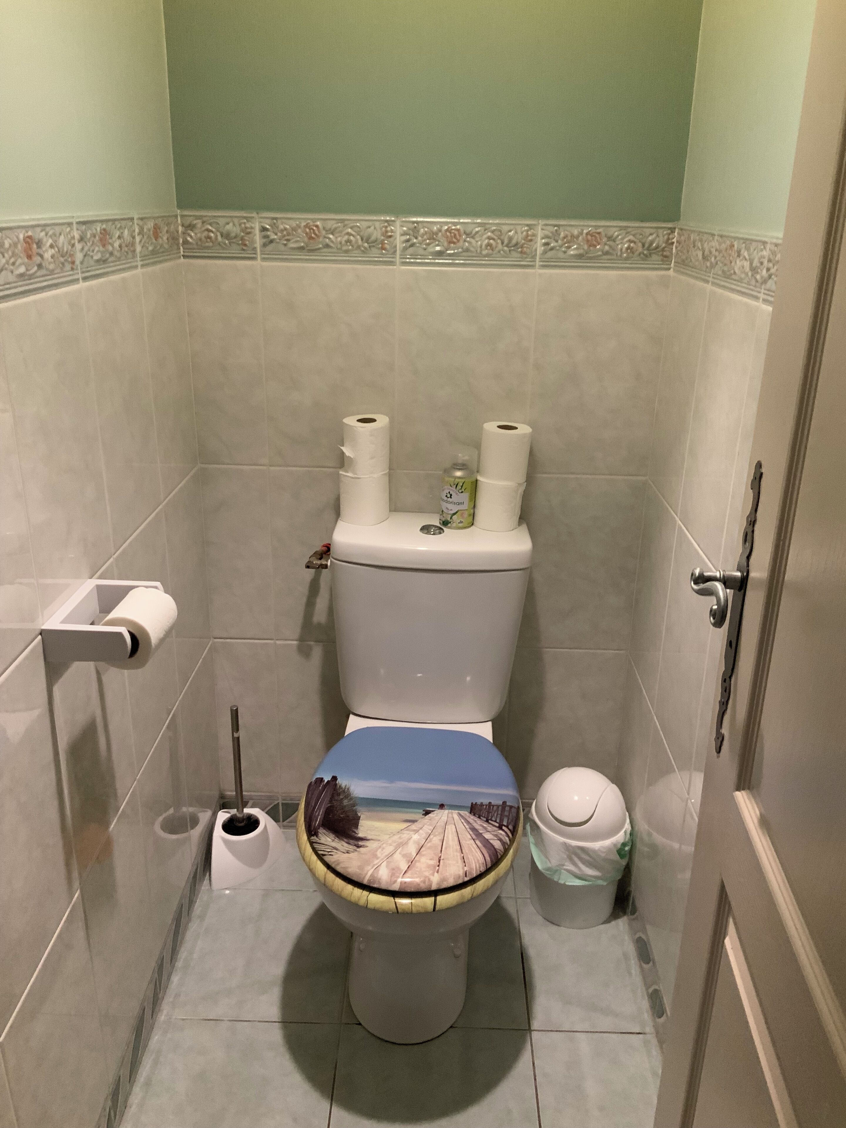 A bathroom with a toilet, a toilet paper holder, a trash bin, and a bidet.