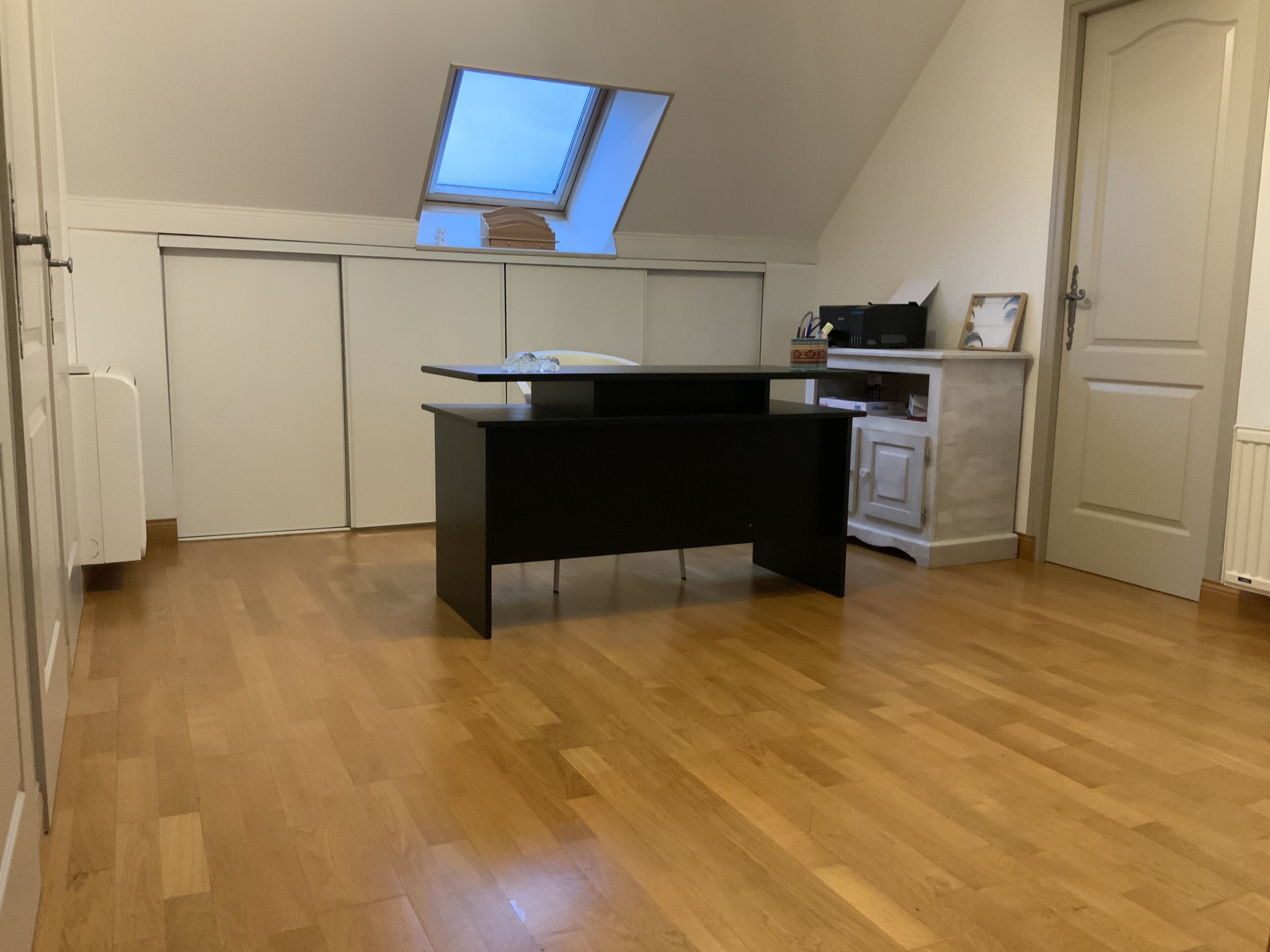 Ein Zimmer mit schrägem Dach, einem Oberlicht, einem schwarzen Schreibtisch, einem weißen Schrank und einer weißen Tür.