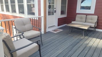 Une terrasse en bois avec des meubles d’extérieur, une porte blanche et des fenêtres.