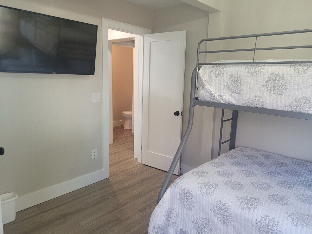 A room with a bunk bed, a television mounted on the wall, and a door leading to a bathroom.