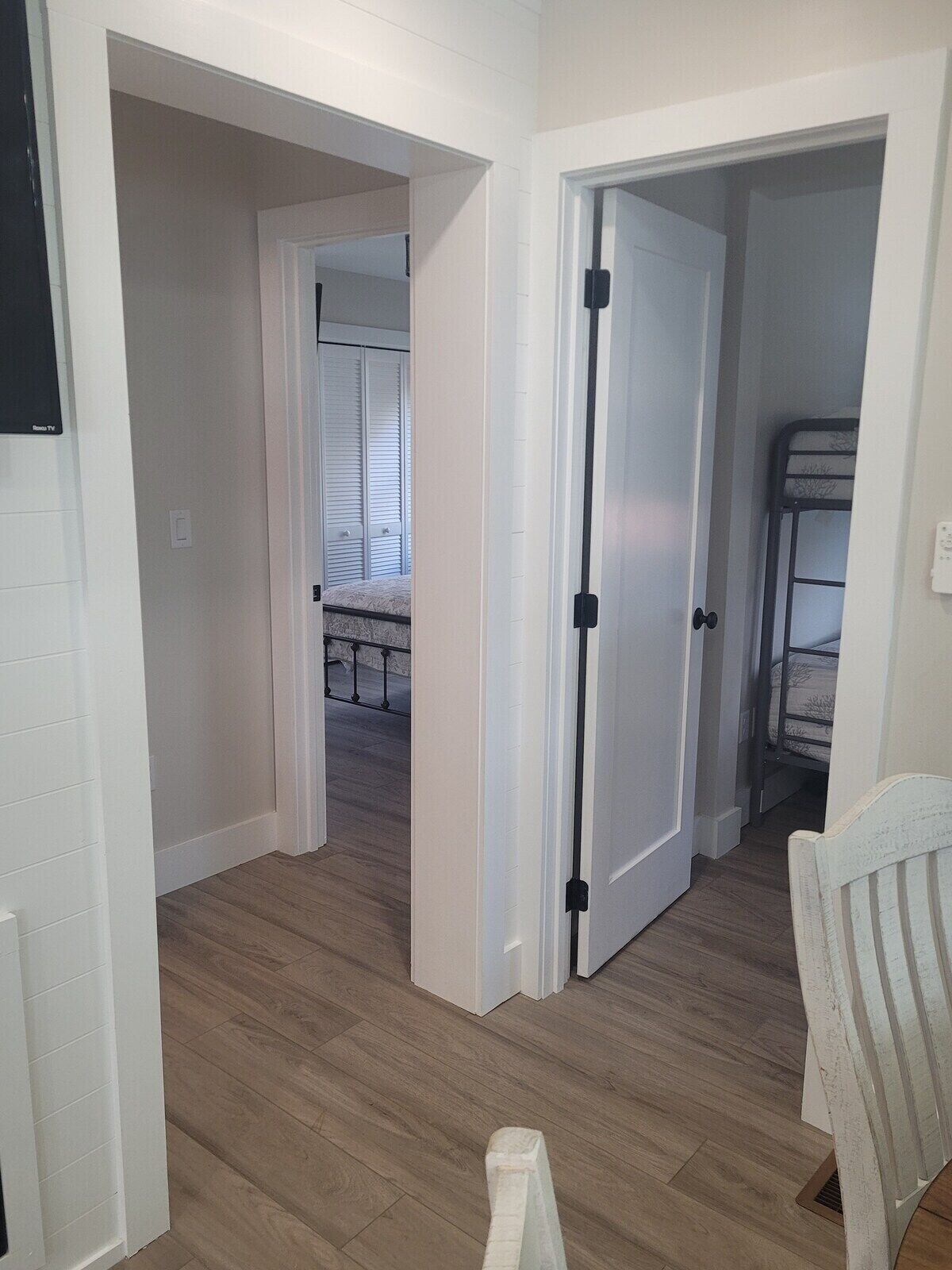 A hallway with wooden flooring, white walls, and a door leading to a room with a bunk bed.