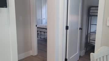 A hallway with wooden flooring, white walls, and a door leading to a room with a bunk bed.