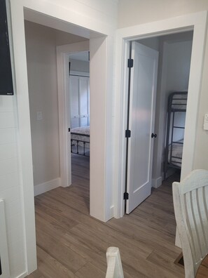 A hallway with wooden flooring, white walls, and a door leading to a room with a bunk bed.
