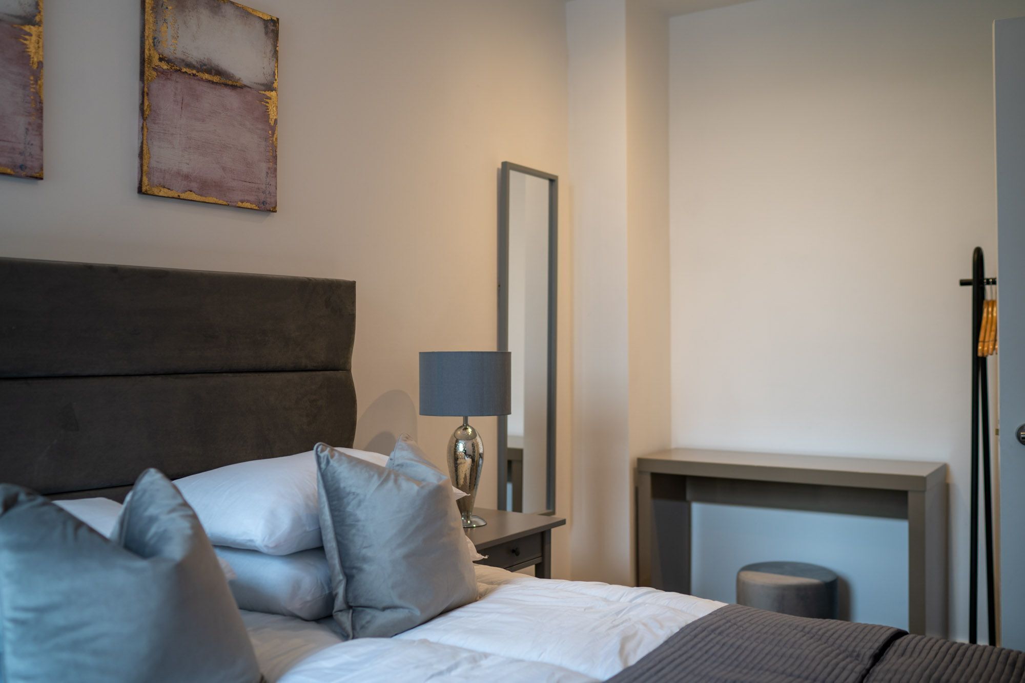 A modern bedroom with a large bed, a bedside table with a lamp, a mirror, and a fireplace.
