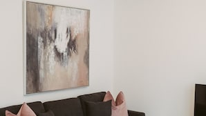 Ein modernes Wohnzimmer mit einem grauen Ecksofa, einem großen abstrakten Gemälde und einem Flachbildfernseher auf einem weißen Lowboard.