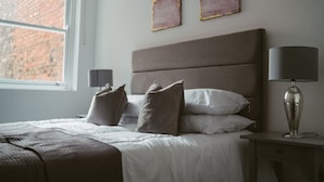 Ein ordentlich bezogenes Bett mit Kissen, einer Nachttischlampe und Bildern an der Wand.