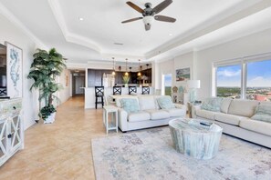 A spacious living room with a ceiling fan, a dining area, and a view of the city. - Beachfront Escape: Sleeps 10, Incredible Views! (Orange Beach)