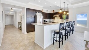 A modern kitchen with a large island, dark cabinets, and pendant lighting.