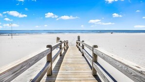 A wooden pier leading to a beach with a clear sky.