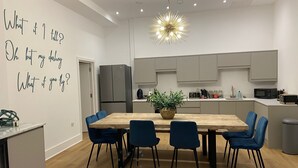 A modern kitchen with a dining area, featuring a wooden table, blue chairs, a hanging light fixture, and a refrigerator.