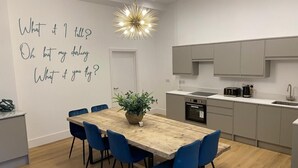 A modern kitchen with a wooden dining table, blue chairs, and a pendant light.
