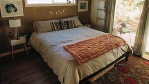 A bedroom with a large bed, a window, a nightstand, and a patterned rug. - Cardiff Hope House with Ocean View (Encinitas)