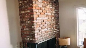 A living room with a brick fireplace, a sofa, a lamp, and a potted plant. - Cardiff Hope House with Ocean View (Encinitas)