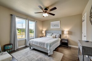 A bedroom with a bed, two bedside tables, a ceiling fan, a window with curtains, and a door.