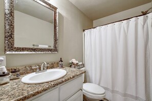 A bathroom with a granite countertop sink, a toilet, a shower curtain, and a mirror with a mosaic frame.