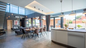 A modern kitchen with a central island, dining area with chairs, and a sofa. - Luxury Villa Aurealis with Pool (Ližnjan)