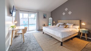 A bedroom with a bed, bedside tables, a desk, and a chair. There is a window with curtains, a wall-mounted TV, and decorative wall art. - Family 3BR POOL Home/ KING BED Suite/ BILLIARD TABLE/ Sleeps 9/near Yaamava' (Rialto)