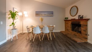 A dining area with a brick fireplace, a table with chairs, a potted plant, and a painting on the wall. - Family 3BR POOL Home/ KING BED Suite/ BILLIARD TABLE/ Sleeps 9/near Yaamava' (Rialto)