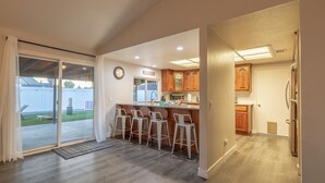 A modern kitchen with wooden cabinets, a bar area with stools, and a sliding glass door leading to a patio. - Family 3BR POOL Home/ KING BED Suite/ BILLIARD TABLE/ Sleeps 9/near Yaamava' (Rialto)