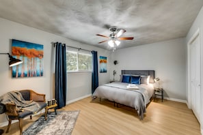 Une chambre à coucher comprenant un lit, une table de chevet, une chaise, un ventilateur de plafond et des œuvres d’art accrochées aux murs.