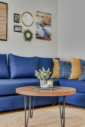 Un canapé bleu, une table basse ronde en bois placée devant, un tableau encadré et un miroir fixé au mur.