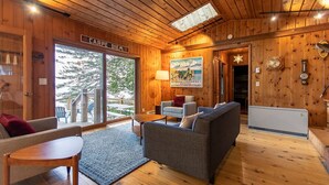 Interior acogedor de una cabaña con techo de madera, un sofá, una mesa y un ventanal con vistas al exterior.