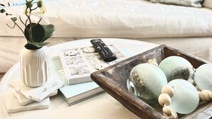 Una sala de estar con un sofá blanco, dos lámparas, una bandeja con adornos y un florero con flores.