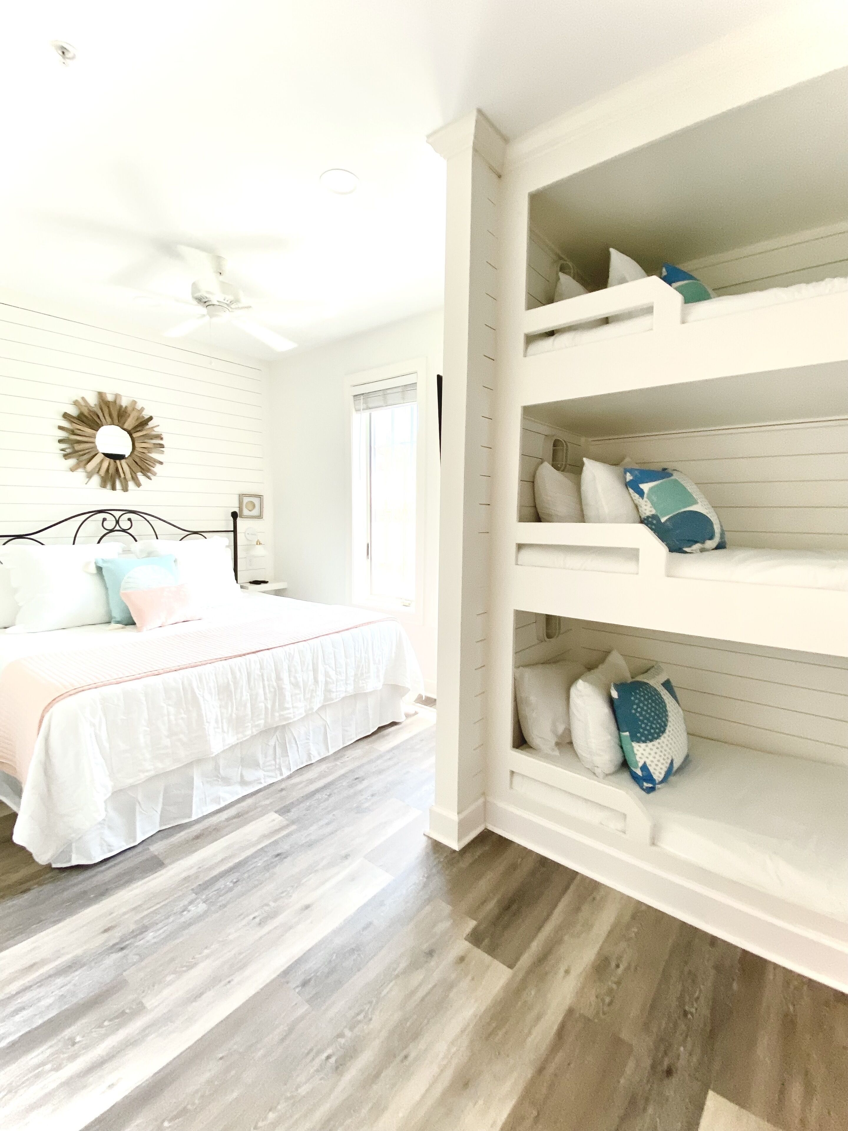 Een slaapkamer met een bed, een witte muur met een zonnespiegel en een ingebouwde kastenwand met kussens.