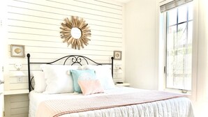 Un dormitorio con cama, mesita de noche, espejo en la pared y ventana.