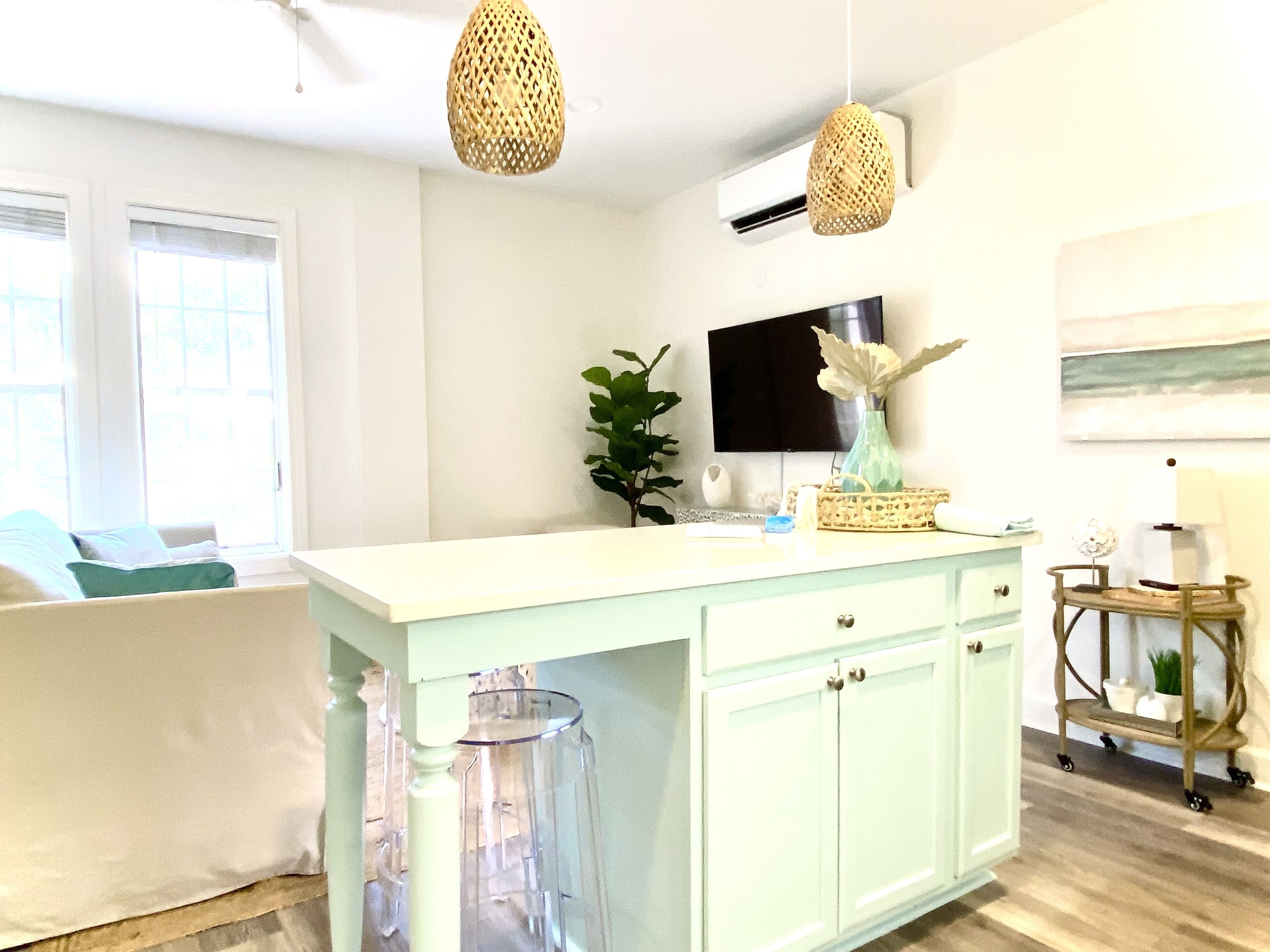 A bright kitchen with a white island, a TV mounted on the wall, and a window with blinds.