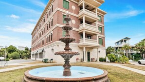 Un edificio de varios pisos con una fuente central, un balcón en el nivel superior y un césped bien cuidado.