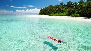 Eine Person treibt an einem Strand mit klarem türkisblauem Wasser und weißem Sand.