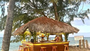 Eine Strandbar mit einem Reetdach, Holzstühlen und Blick aufs Meer.