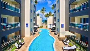 Ein modernes Hotel mit einem zentral gelegenen Pool, mehreren Balkonen und Blick auf Palmen.