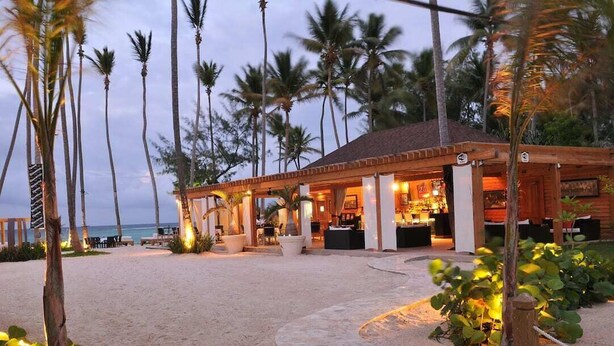 Ein Strandhotel mit überdachtem Außenbereich, Palmen und einem Sandstrand.