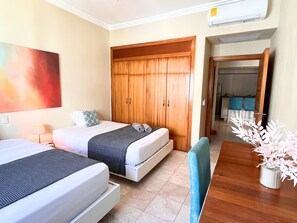 A hotel room with two beds, a wooden wardrobe, a dining table with chairs, and a vase with white flowers. - Chic Beachfront Apartment - Private Beach Access (Punta Cana)