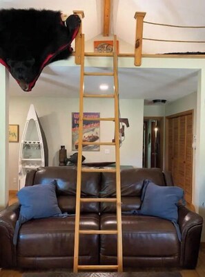 Une échelle en bois dans un salon, avec un canapé en cuir marron et des coussins bleus.