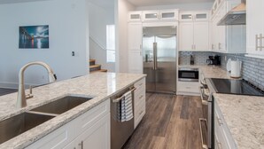 A modern kitchen with white cabinets, stainless steel appliances, and a granite countertop. - Luxury Waterfront Estate—Pool, Spa, Game Lounge, 2 Docks & Ramp Access—Gulfside (Marathon)