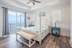 Une chambre à coucher avec un lit à baldaquin, un banc, une table de chevet de couleur turquoise et une vue sur l’océan par une porte coulissante.