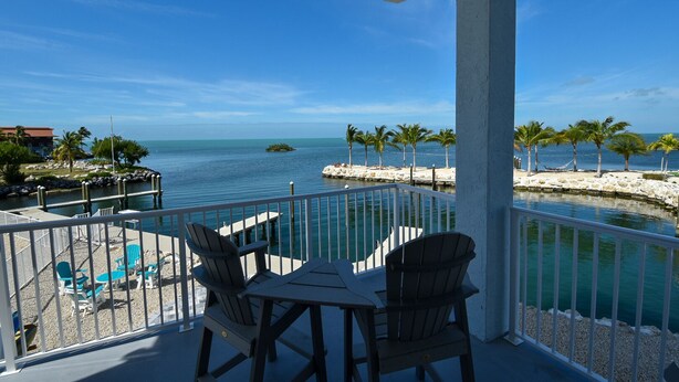 A balcony with a view of the sea, featuring a table and chairs, and a pool area with lounge chairs. - Luxury Waterfront Estate—Pool, Spa, Game Lounge, 2 Docks & Ramp Access—Gulfside (Marathon)