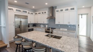 A modern kitchen with white cabinets, a large island with bar stools, stainless steel appliances, and a tiled backsplash. - Luxury Waterfront Estate—Pool, Spa, Game Lounge, 2 Docks & Ramp Access—Gulfside (Marathon)