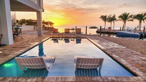 A swimming pool with lounge chairs, a sunset view, and a beach in the background. - Luxury Waterfront Estate—Pool, Spa, Game Lounge, 2 Docks & Ramp Access—Gulfside (Marathon)