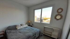 Een slaapkamer met een bed, nachtkastje, lamp, raam en een radiator.
