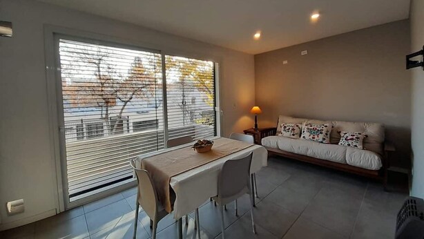 Een moderne woonkamer met een eettafel en een bank, grote ramen en een plafondlamp.