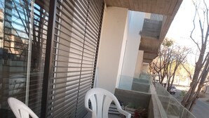 Een balkon met twee witte kunststof stoelen en een kleine tafel, een glazen hekwerk en planten in potten.