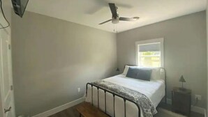 Un dormitorio con una cama individual, ventilador de techo, ventana y una mesita de noche pequeña.