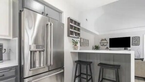 A modern kitchen with stainless steel appliances, a white countertop, two stools, and a flat-screen TV mounted on the wall. - Pet Friendly Paso Robles Wine Retreat (Templeton)