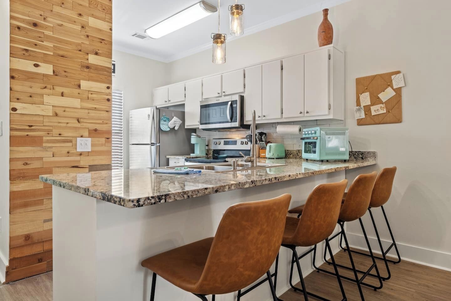 Una cocina moderna con armarios blancos, encimera de granito y una isla central con taburetes de bar.
