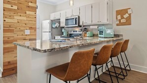 A modern kitchen with white cabinets, a granite countertop, and a central island with bar stools. - Location, location, location! Steps to the pool and just a 5-minute walk to the beach 🏖️💦 (Miramar Beach)